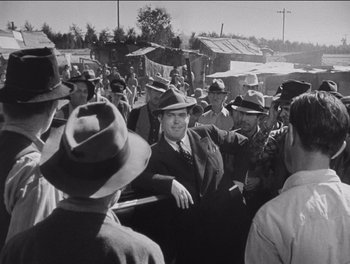Movie still from “The Grapes of Wrath” (1940), directed by John Ford – A group of men standing next to each other in hats; Medium shot, Over the shoulder angle