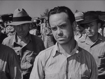 Movie still from “The Grapes of Wrath” (1940), directed by John Ford – Black and white photograph of a man in a crowd; Medium shot, Low angle