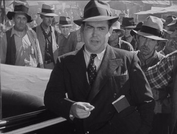 Movie still from “The Grapes of Wrath” (1940), directed by John Ford – A man in a suit and hat is holding a cigarette; Medium shot, Low angle