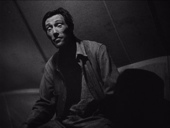 Movie still from “The Grapes of Wrath” (1940), directed by John Ford – Black and white photograph of a man sitting on a bench; Close Up shot, Low angle