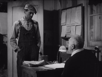 Movie still from “The Grapes of Wrath” (1940), directed by John Ford – An old photo of a man and an older man at a desk; Medium shot, Over the shoulder angle