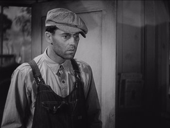 Movie still from “The Grapes of Wrath” (1940), directed by John Ford – A man wearing a hat and overalls standing in front of a door; Medium shot, Low angle