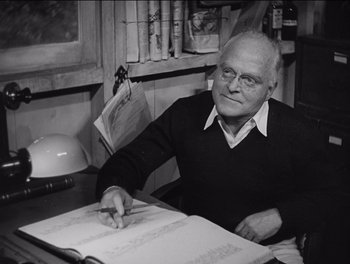 Movie still from “The Grapes of Wrath” (1940), directed by John Ford – An older man sitting at a table with a book; Medium shot, High angle