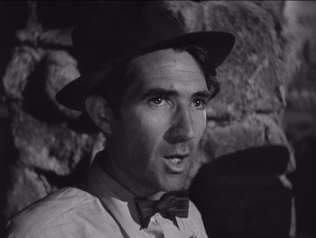 Movie still from “The Grapes of Wrath” (1940), directed by John Ford – A man wearing a hat and a bow tie in front of a stone wall; Close Up shot, Low angle