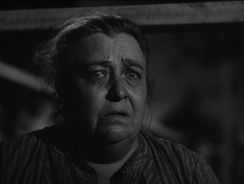Movie still from “The Grapes of Wrath” (1940), directed by John Ford – An older woman looking sad while standing in a dark room; Close Up shot, Low angle