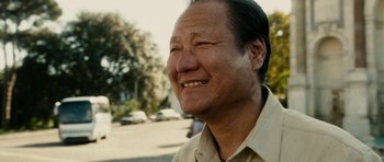 Movie still from “The Great Beauty” (2013), directed by Paolo Sorrentino – An older asian man smiling for the camera outside; Close Up shot, Low angle