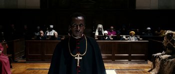 Movie still from “The Great Beauty” (2013), directed by Paolo Sorrentino – A man wearing a priest's outfit in front of a group of people in a court room; Medium shot, Low angle