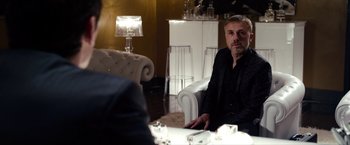 Movie still from “The Green Hornet” (2011), directed by Michel Gondry – A man sitting at a table in front of a lamp; Medium shot, Over the shoulder angle