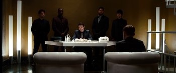 Movie still from “The Green Hornet” (2011), directed by Michel Gondry – A group of men standing around a table with a man sitting at the top of the table; Wide shot, Over the shoulder angle
