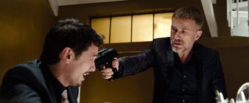 Movie still from “The Green Hornet” (2011), directed by Michel Gondry – A man in a black suit is holding a gun up to his face; Medium shot, Over the shoulder angle