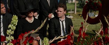 Movie still from “The Green Hornet” (2011), directed by Michel Gondry – A man in a suit and tie sitting next to flowers; Medium shot, Over the shoulder angle