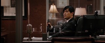 Movie still from “The Green Hornet” (2011), directed by Michel Gondry – A man sitting at a desk holding a guitar; Medium shot, Over the shoulder angle