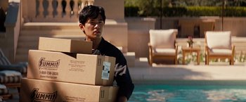 Movie still from “The Green Hornet” (2011), directed by Michel Gondry – A man carrying boxes near a swimming pool; Medium shot, Over the shoulder angle
