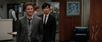 Movie still from “The Green Hornet” (2011), directed by Michel Gondry – Two men in suits standing next to each other in a room; Medium shot, Over the shoulder angle