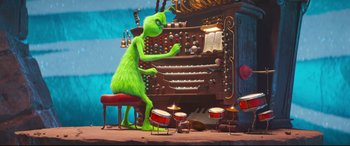 Movie still from “The Grinch” (2018), directed by Yarrow Cheney – The grinch is playing the organ at a christmas party; Wide shot, High angle