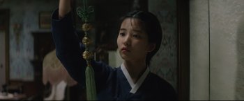 Movie still from “The Handmaiden” (2016), directed by Park Chan-wook – A young asian woman holding a green and gold ornament; Close Up shot, Low angle