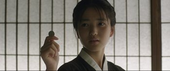 Movie still from “The Handmaiden” (2016), directed by Park Chan-wook – A young asian woman holding a coin in front of a window; Close Up shot, Over the shoulder angle