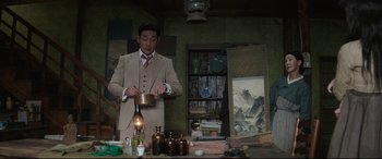 Movie still from “The Handmaiden” (2016), directed by Park Chan-wook – A man in a tan suit is pouring liquid into a pot; Medium shot, Low angle