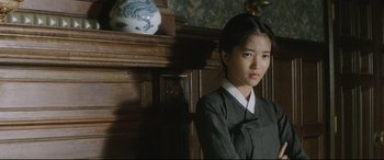 Movie still from “The Handmaiden” (2016), directed by Park Chan-wook – A young asian woman standing in front of a wall; Medium shot, Over the shoulder angle