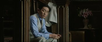 Movie still from “The Handmaiden” (2016), directed by Park Chan-wook – A man sitting on a chair wearing a dress shirt and a tie; Medium shot, Low angle