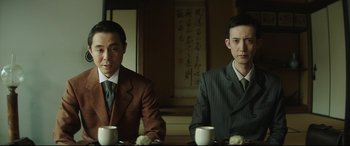 Movie still from “The Handmaiden” (2016), directed by Park Chan-wook – Two men in suits sitting at a table with cups; Medium shot, Low angle