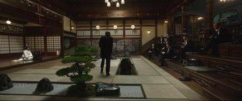 Movie still from “The Handmaiden” (2016), directed by Park Chan-wook – A man standing in front of a group of people; Wide shot, High angle