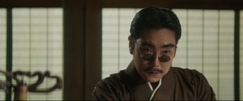 Movie still from “The Handmaiden” (2016), directed by Park Chan-wook – A man with a goatee and round glasses; Close Up shot, Low angle