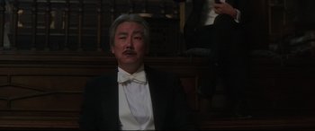 Movie still from “The Handmaiden” (2016), directed by Park Chan-wook – An older man in a tuxedo sitting in front of a wall; Medium shot, Low angle