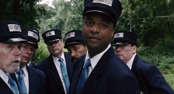 Movie still from “The Happening” (2008), directed by M. Night Shyamalan – A group of men in suits and ties standing next to each other; Medium shot, Low angle