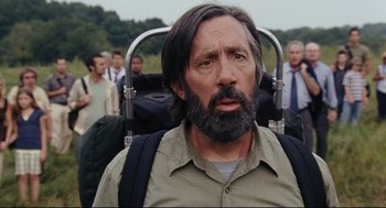 Movie still from “The Happening” (2008), directed by M. Night Shyamalan – A man with long hair and a beard is standing in front of a group of people; Close Up shot, Low angle