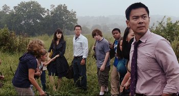 Movie still from “The Happening” (2008), directed by M. Night Shyamalan – A group of people standing in the grass; Medium shot, Over the shoulder angle