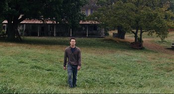 Movie still from “The Happening” (2008), directed by M. Night Shyamalan – A man standing in the grass near a house; Wide shot, High angle