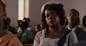 Movie still from “The Help” (2011), directed by Tate Taylor – A woman with a hat sitting in front of other people; Close Up shot, Low angle