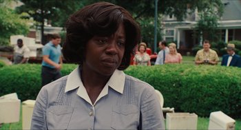Movie still from “The Help” (2011), directed by Tate Taylor – A woman in a gray shirt is standing in front of a crowd; Close Up shot, Over the shoulder angle
