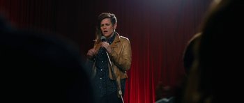 Movie still from “The Hero” (2017), directed by Brett Haley – A woman standing on a stage holding a microphone; Medium shot, Over the shoulder angle