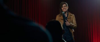 Movie still from “The Hero” (2017), directed by Brett Haley – A woman standing on a stage holding a microphone; Medium shot, Over the shoulder angle