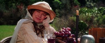 Movie still from “Practical Magic” (1998), directed by Griffin Dunne – A woman wearing a straw hat sitting next to a table with grapes on it; Close Up shot, Over the shoulder angle