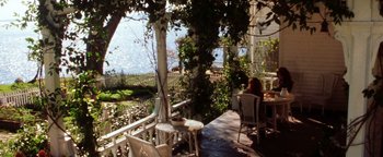 Movie still from “Practical Magic” (1998), directed by Griffin Dunne – A woman sitting on a porch with a view of the ocean; Extreme Wide shot, High angle