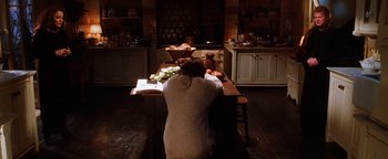 Movie still from “Practical Magic” (1998), directed by Griffin Dunne – A woman sitting at a table in a kitchen preparing a meal; Wide shot, High angle