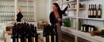 Movie still from “Practical Magic” (1998), directed by Griffin Dunne – A woman in an apron standing in front of a shelf filled with wine bottles; Medium shot, High angle