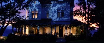 Movie still from “Practical Magic” (1998), directed by Griffin Dunne – A house with a porch lit up at night time; Wide shot, Low angle