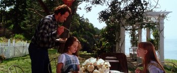Movie still from “Practical Magic” (1998), directed by Griffin Dunne – A woman sitting at a table with a man standing next to her; Medium shot, Over the shoulder angle