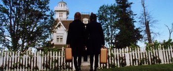Movie still from “Practical Magic” (1998), directed by Griffin Dunne – Two women holding suitcases are standing in front of a house; Wide shot, Low angle