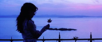 Movie still from “Practical Magic” (1998), directed by Griffin Dunne – A woman holding a leaf in front of a body of water; Medium shot, Low angle