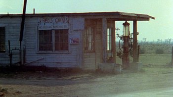 Movie still from “The Hills Have Eyes” (1977), directed by Wes Craven – An abandoned gas station in the middle of a deserted road; Wide shot, High angle