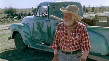 Movie still from “The Hills Have Eyes” (1977), directed by Wes Craven – An older man in a cowboy hat standing in front of an old truck; Medium shot, Low angle
