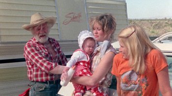 Movie still from “The Hills Have Eyes” (1977), directed by Wes Craven – A woman holding a baby in her arms while standing next to a man and woman; Medium shot, Over the shoulder angle