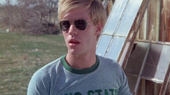 Movie still from “The Hills Have Eyes” (1977), directed by Wes Craven – A young man wearing sunglasses and a t - shirt; Close Up shot, Low angle