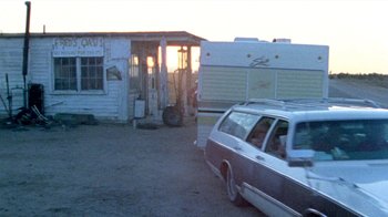 Movie still from “The Hills Have Eyes” (1977), directed by Wes Craven – An rv parked in front of a building with a car parked in front of it; Wide shot, Low angle