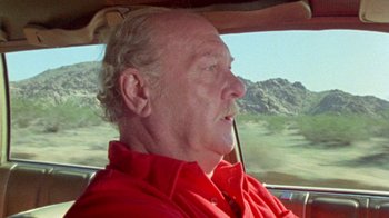 Movie still from “The Hills Have Eyes” (1977), directed by Wes Craven – An older man wearing a red shirt driving a car; Close Up shot, Low angle